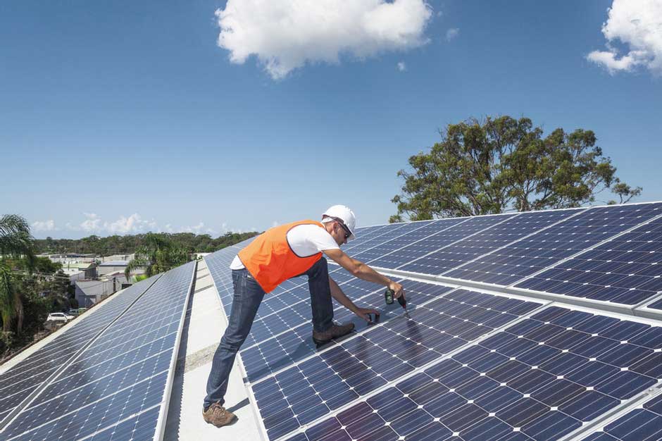 Worker finishing installing solar panels on a large roof